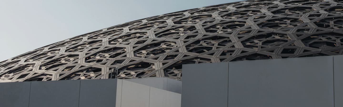 The grey dome of the Louvre Abu Dhabi seen from the water.