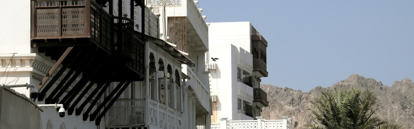 Carved timber balconies on the white facades of the Muttrah Corniche, Muscat.