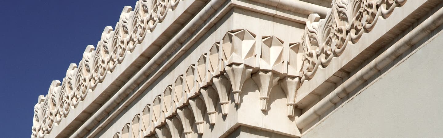 Carved white facade detail on a Sharjah building against a clear sky.